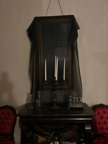 A 19th century mirror hangs on a wall, draped with black fabric