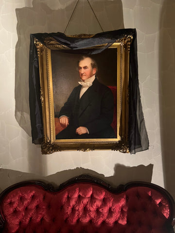 19th century portrait hangs on a wall with black fabric draped around it