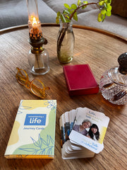 Decks of Remembering A Life Journey Cards and Have the Talk of a Lifetime Conversation Cards on a table with a pair of glasses, a book and a small decanter